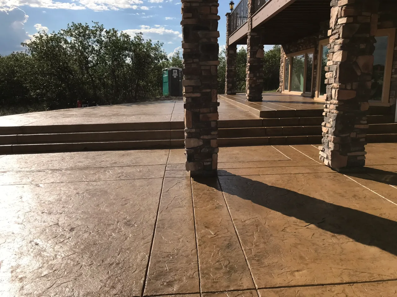 Golden stamped concrete patio with wide steps under a stone-column deck in El Paso County, CO